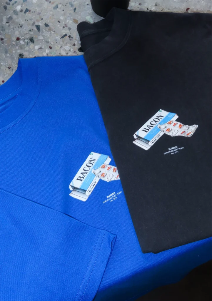Blue and black T-shirts with bacon pack design, laid on terrazzo floor.