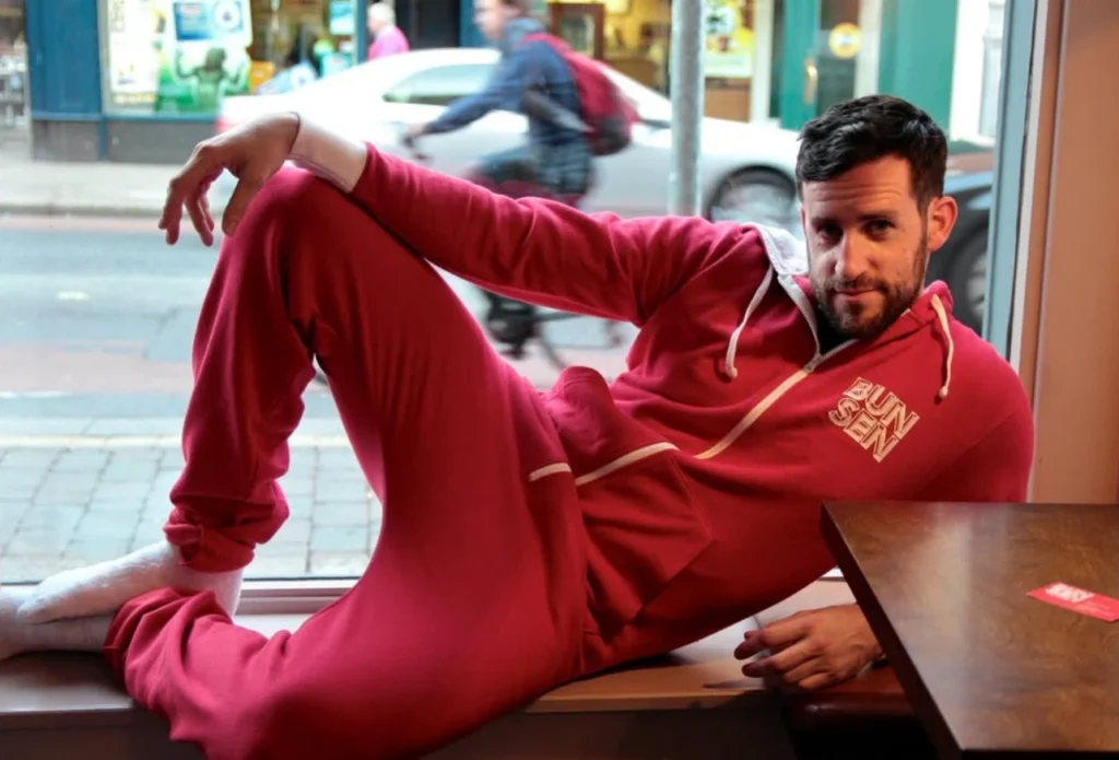 Man in a red onesie lounging by a window in a cosy cafe setting, with street view in the background.